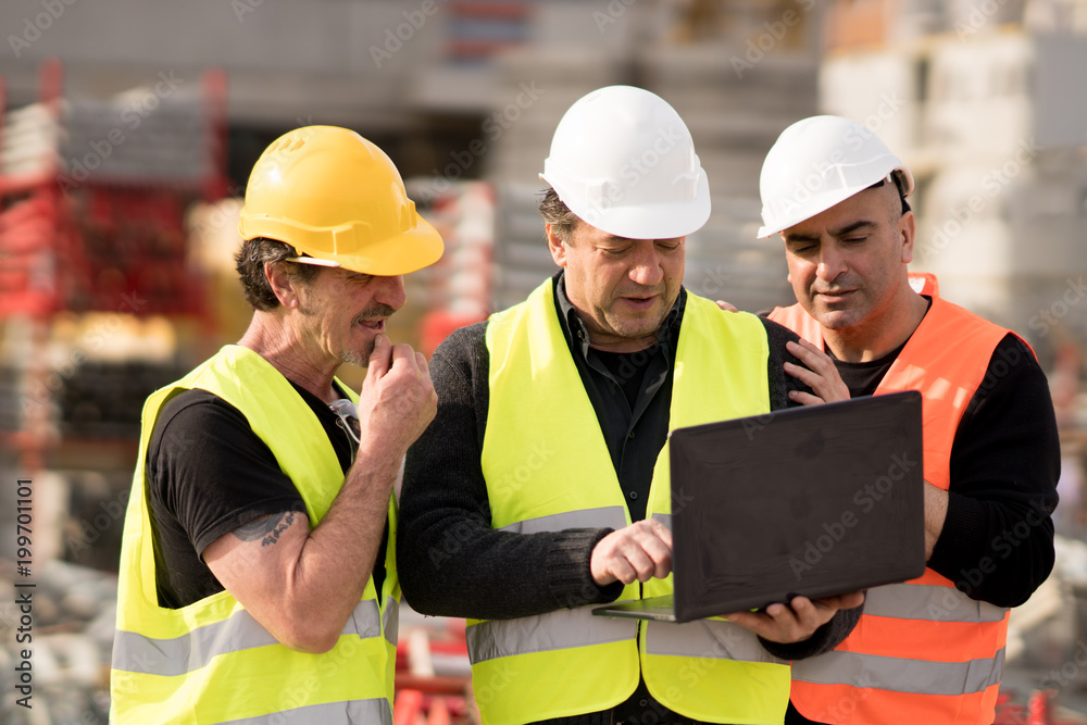 Construction site manager giving instructions using a laptop digital computer Construction site manager giving instructions using a laptop digital computer