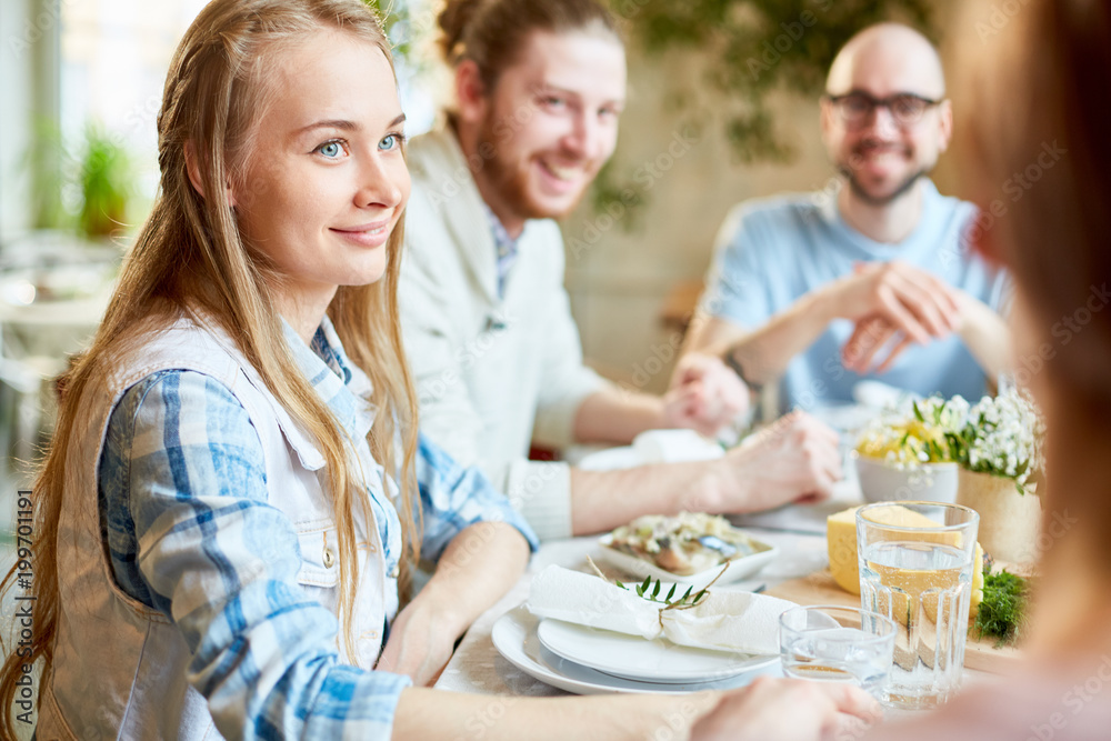 Happy girl and two guys listening to their friend while gathered by served festive table