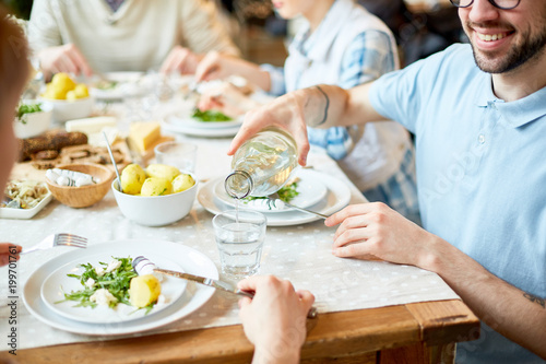 Photography Young man pouring fresh lemonade into glass of his friend while having dinner by