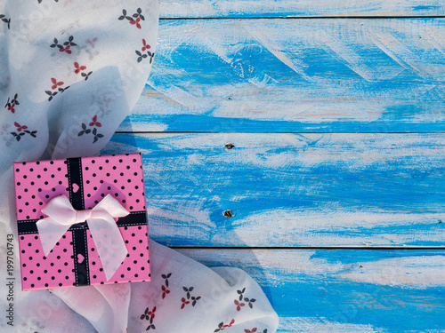 One pink gift box on white scarf on blue wood table