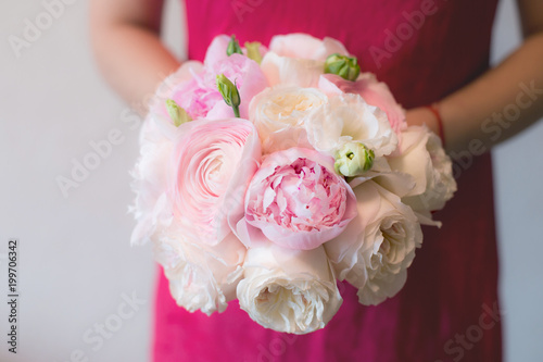 A woman in a pink dress is holding amazing bridal bouquet of pink peonies Sarah Bernhardt, ranunculuses Hanoi, Keira roses and white Eustoma. Wedding floristry photo