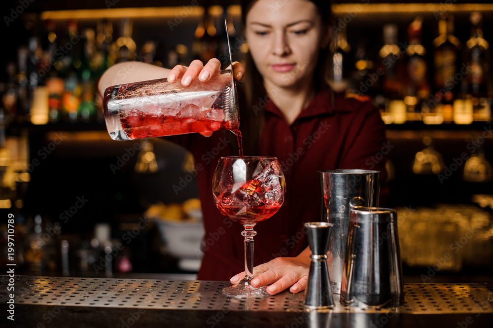 Bartender girl pouring a delicious light red cocktail