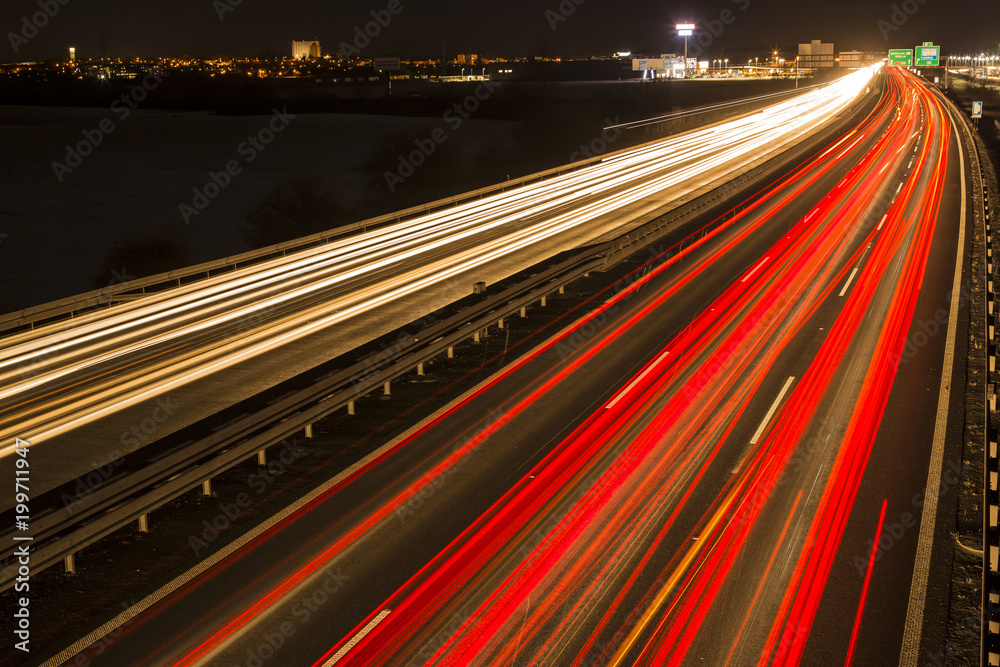 Night scene of motion blurred light tracks glowing to the darkness of highway traffic to the city just after sunset. Creative long time exposure diagonal composed photography.