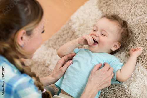 Foto Loving mom tickling her little baby kid on carpet at home