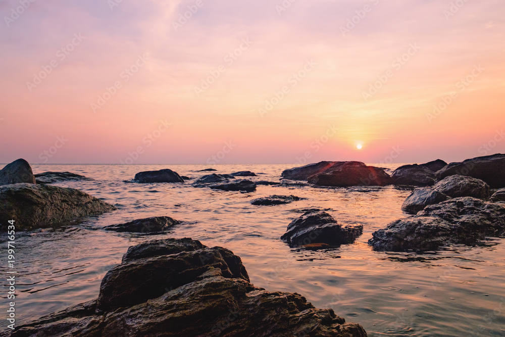 Obraz premium Tropical colourful sunset on the beach of Koh Chang island, Gulf of Siam, Thailand. View of dark night sea with protruding stones.