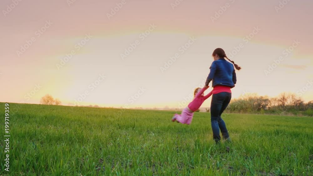 Young mommy is playing with her daughter in a picturesque place. It circles her around him, at sunset Young mommy is playing with her daughter in a picturesque place. It circles her around him, at sunset