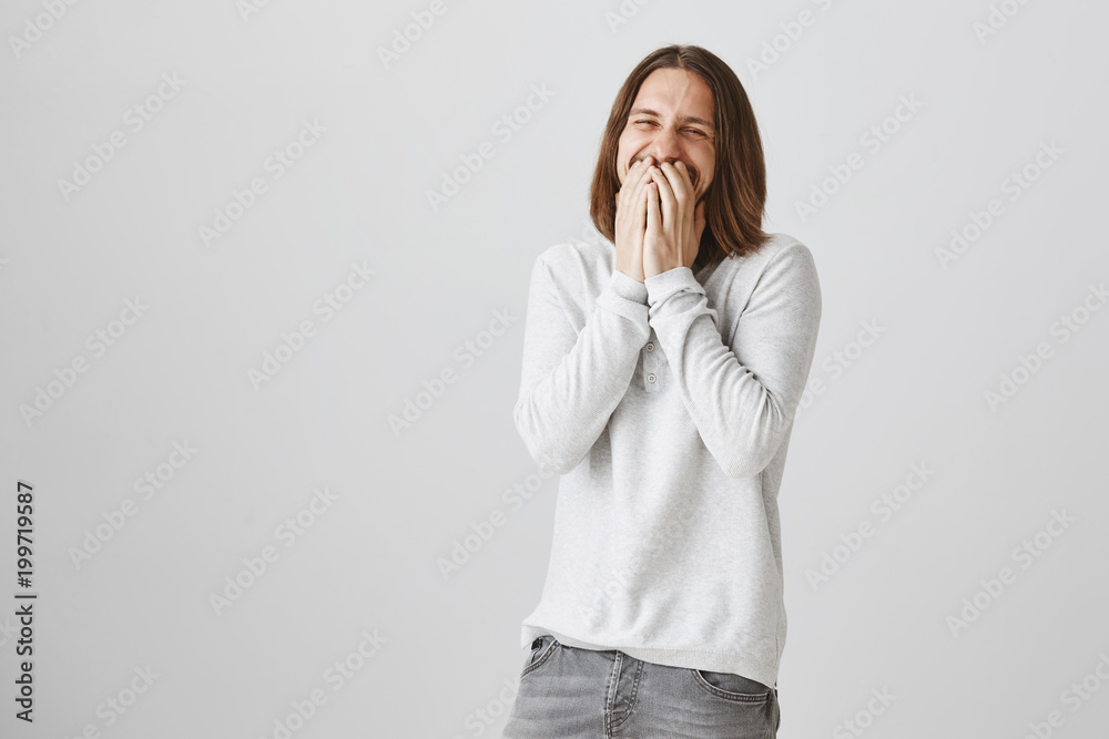 Laughing out loud from positive emotions. Portrait of good-looking caucasian bearded guy with long hair chuckling, covering mouth with hands, being over-emotional from happiness and excitement Laughing out loud from positive emotions. Portrait of good-looking caucasian bearded guy with long hair chuckling, covering mouth with hands, being over-emotional from happiness and excitement