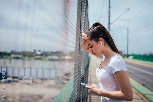 Girl leaning on wire fence listening to music on the phone.