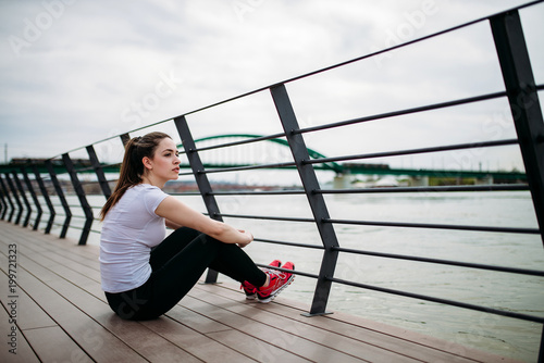 Runner girl taking a break. Sitting at city quay, looking away. photo