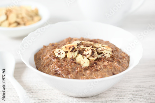 Chocolate oatmeal or oat porridge with toasted almond slices and grated chocolate on top served in small bowl, photographed with natural light (Selective Focus, Focus in the middle of the porridge)