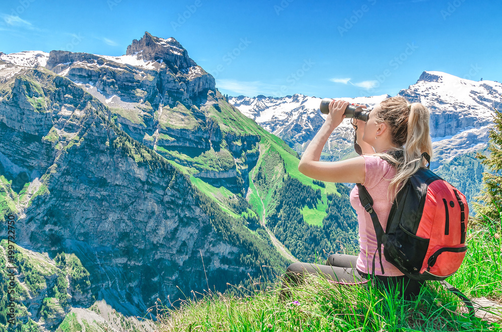 girl traveler examines through the binoculars the peak of Mount Engelberg, against the backdrop of the mountain peaks, admires the nature and the mountain scenery of Switzerland