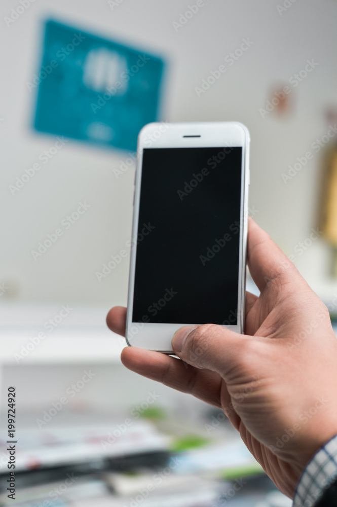 Closeup view of a man's hand online working on smart phone with blank display background over light indoors interior. Using internet digital device as modern design communication technology lifestyle