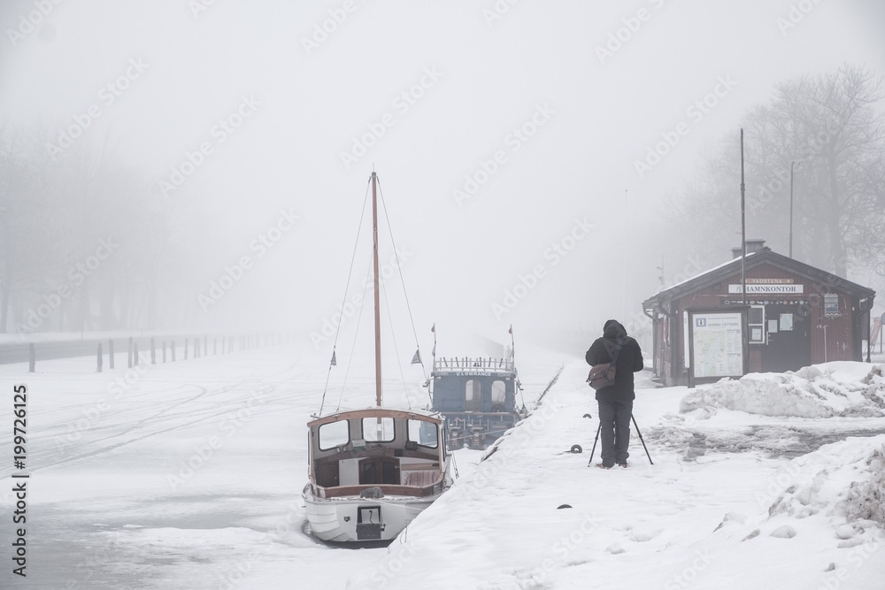 man standing taking pictures on a frozen canal a misty winters day man standing taking pictures on a frozen canal a misty winters day