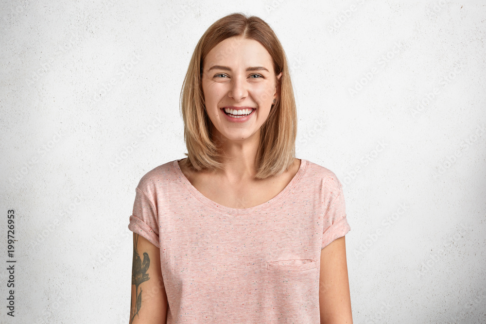 Happy lovely pretty young female model with bobbed hairstyle and shining smile, being in good mood after successful shopping, dressed in casual loose t shirt, isolated over white background. Happy lovely pretty young female model with bobbed hairstyle and shining smile, being in good mood after successful shopping, dressed in casual loose t shirt, isolated over white background.