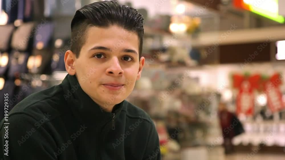 Portrait of a stylish brunette man with crew haircut sitting and looking at camera in a glassy shopping mall. He feels happy and confident. Portrait of a stylish brunette man with crew haircut sitting and looking at camera in a glassy shopping mall. He feels happy and confident.