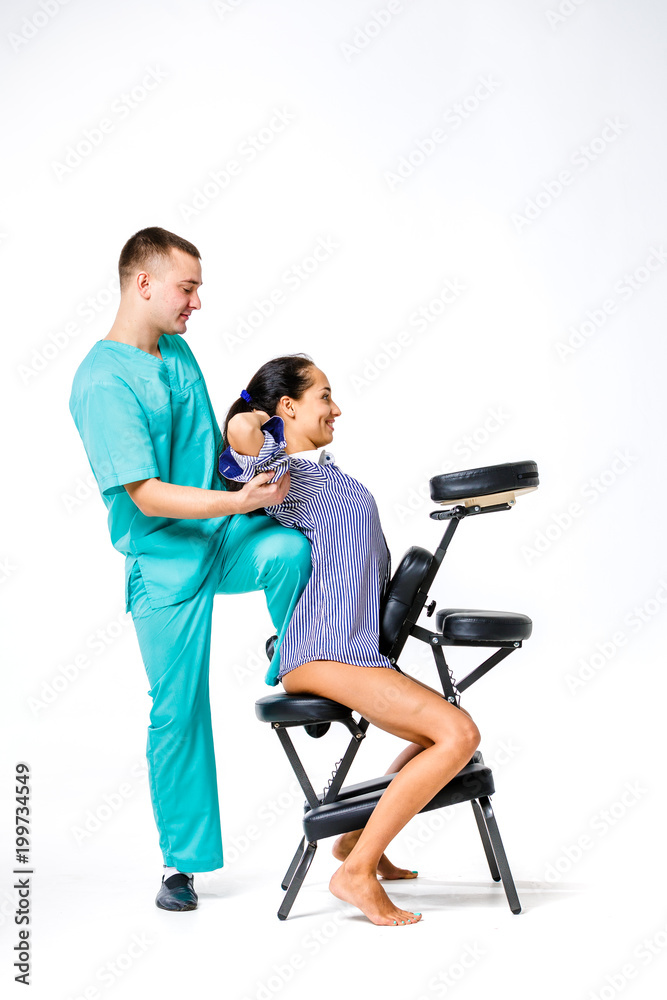 Theme massage and office. young male therapist in blue suit doing back massage with his knee braced in the spine of female worker, business woman in shirt on shiatsu massage chair for fatigue relief Theme massage and office. young male therapist in blue suit doing back massage with his knee braced in the spine of female worker, business woman in shirt on shiatsu massage chair for fatigue relief
