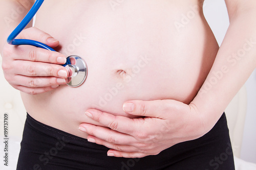 Image of pregnant woman with the stethoscope on the belly listening to the baby's heartbeat