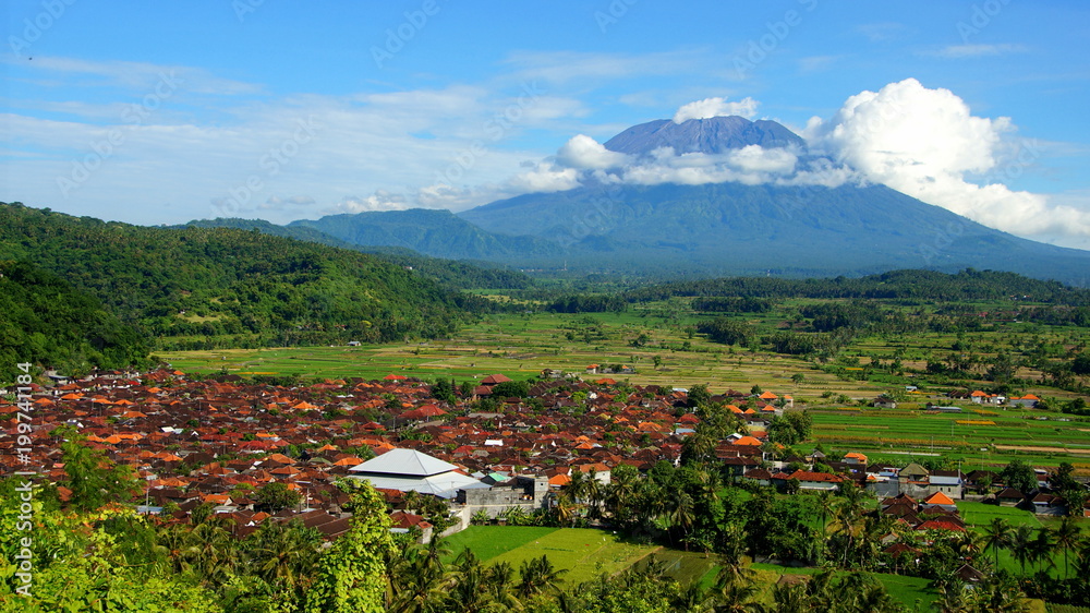 malerisches Dorf zwischen grünen Reisfeldern vor Vulkan Mt.Agung in Bali bei blauen Himmel