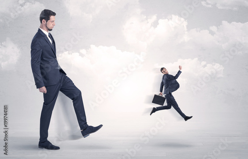 Big businessmen kicking himself as a small employee with cloudy background 