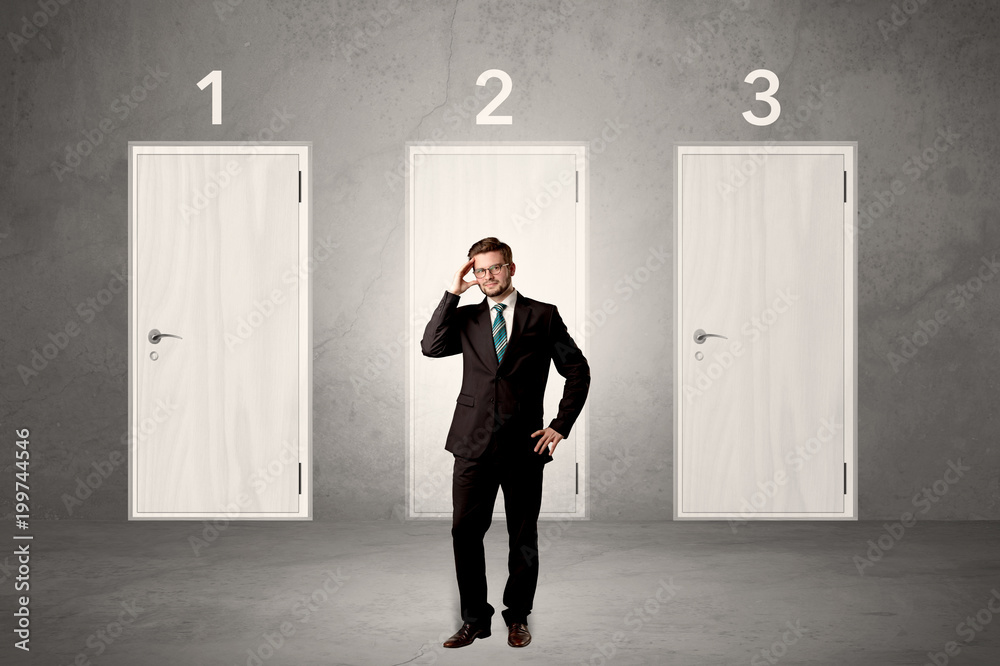 Fototapeta premium Businessman in grey room with three numbered white door behind his back 