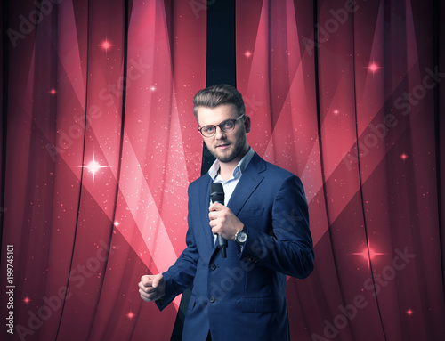 Businessman speaking into microphone with red curtain behind him 