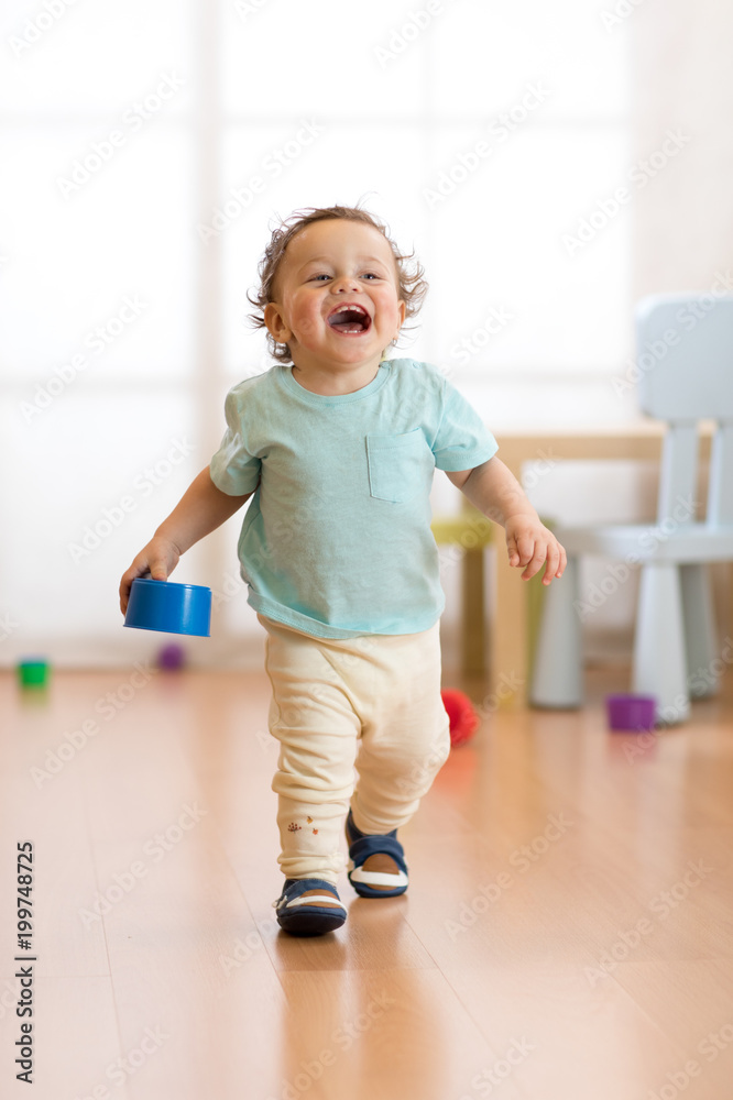 First steps of baby toddler learning to walk in living room. Footwear for little kids.