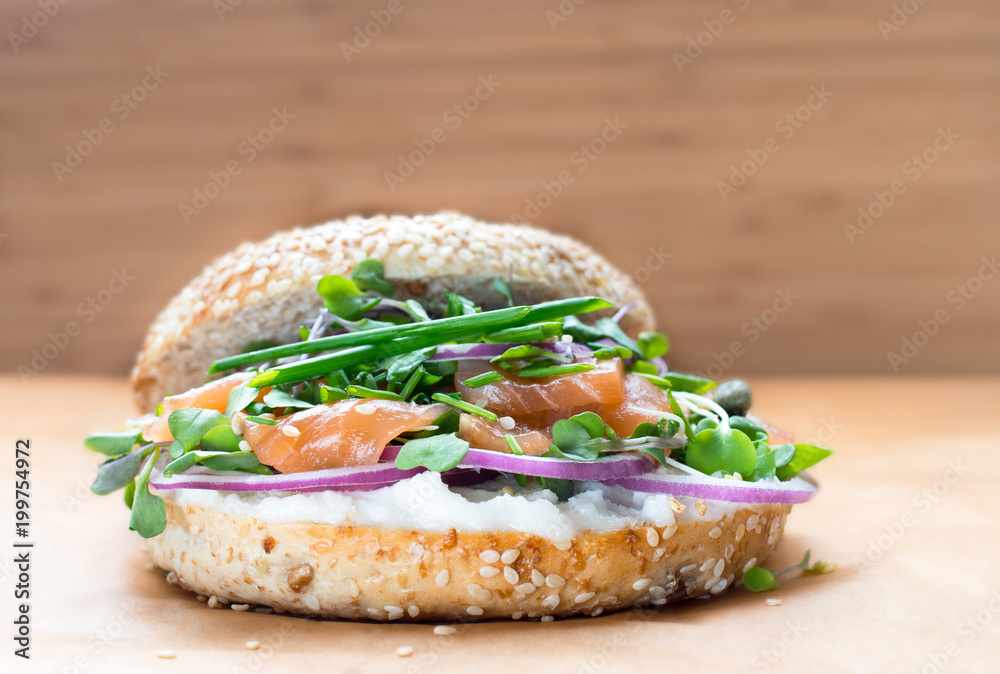 Bagel sandwich with creame cheese, salmon,onion,tomato,greens,chives close-up on a wooden background. Delicious bagel, golden bake color, soft inside, crispy outside. Bagel sandwich with creame cheese, salmon,onion,tomato,greens,chives close-up on a wooden background. Delicious bagel, golden bake color, soft inside, crispy outside.