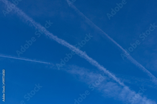 Contrails in blue sky with airplane flying