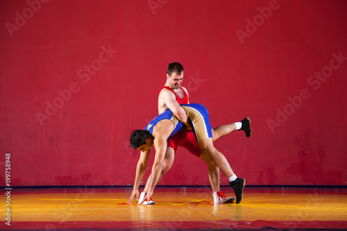 Two strong wrestlers in blue wrestling tights are wrestlng and making a suplex wrestling on a yellow wrestling carpet in the gym. Young man doing grapple.