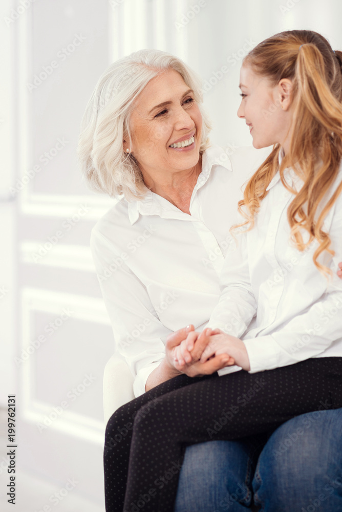 Love you to the moon and back. Adorable moment of loving female grandparent looking into eyes of her granddaughter while a well mannered girl sitting on the lap of her grandmother and beaming.