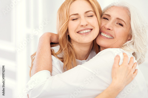 Happiness is homemade. Sunshiny mature daughter and her elderly mom grinning broadly into the camera while embracing and enjoying a happy family moment spent together.