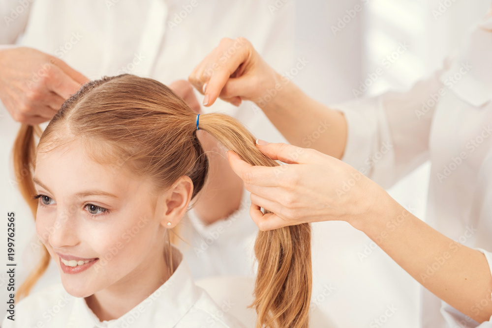Fototapeta premium Every girls routine. Scaled up look on a cheerful girl sitting on a chair while her loveful mother and grandma standing next to her and doing her hair at home.