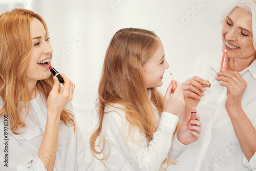 Such a fun time. Radiant little girl spending family time with her beautiful mom and granny and enjoying the moment while applying lips makeup together with them. photo