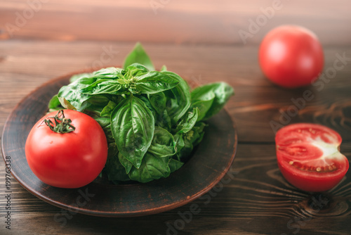 View on a brown wooden table with tomatoes and plate with green basil
