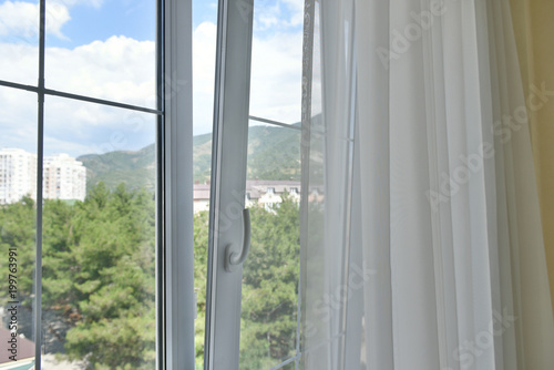 The plastic window is open. Open window with curtains and mountain views © pridannikov