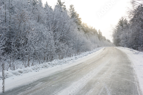 snowy winter asphalt road during blizzard, white forest and white road