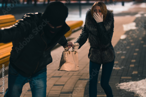 Thief Dangerous man or masked robber with knife attacking shoulder bag. Robber or thief holding knife burglarize to steal the money wallet in woman's bag, while sitting at restaurant and don't careful photo