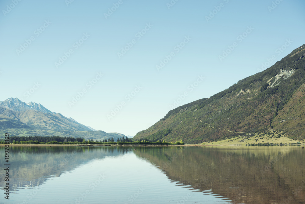 Paisaje y reflejo de bosque y falda de montaña verde a la orilla de un lago en un día despejado