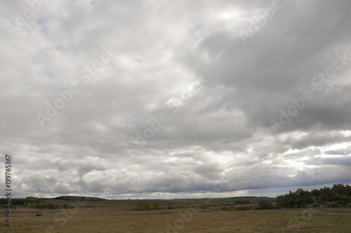 Heavy grey clouds in the cold autumn sky over fields, forests and mountains