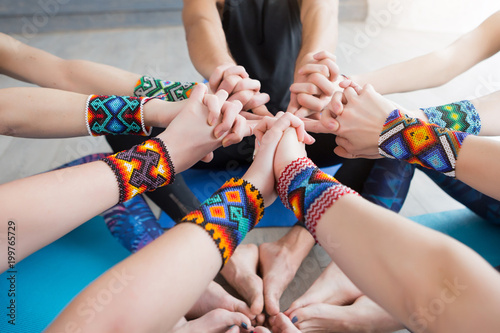 Close up of hands and legs of Group of sporty happy people sitting on the gym floor in a circle together, resting and meditating after yoga class with instructor indoors. Healthy lifestyle concept
