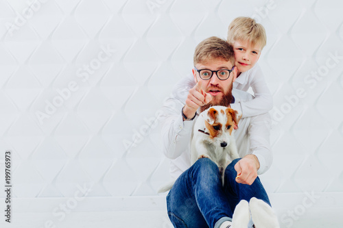 Father and son with puppy dog family making a pyramid on white background. Beard man pointing with a finger at you. Friendship and pet lover concept. Copy space.