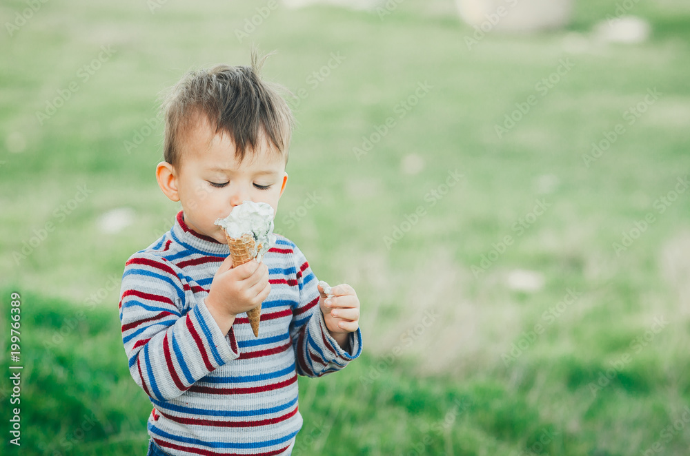 little cute boy eating ice cream three years very appetizing, amid nature, green grass little cute boy eating ice cream three years very appetizing, amid nature, green grass