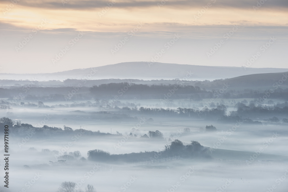 Stunning foggy English rural landscape at sunrise in Winter with layers rolling through the fields Stunning foggy English rural landscape at sunrise in Winter with layers rolling through the fields
