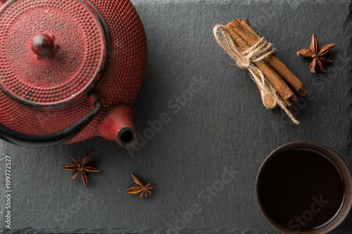 Red iron teapot and traditional ceramic cup of tea over dark texture background.