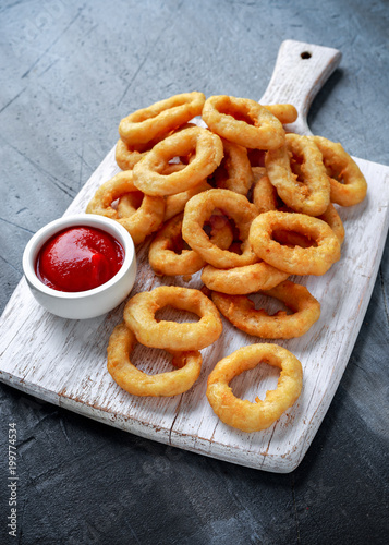 Fried Onion Rings with Ketchup on white cutting board.