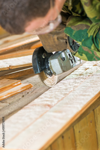 A young carpenter in goggles processes the surface of the boards with a tool