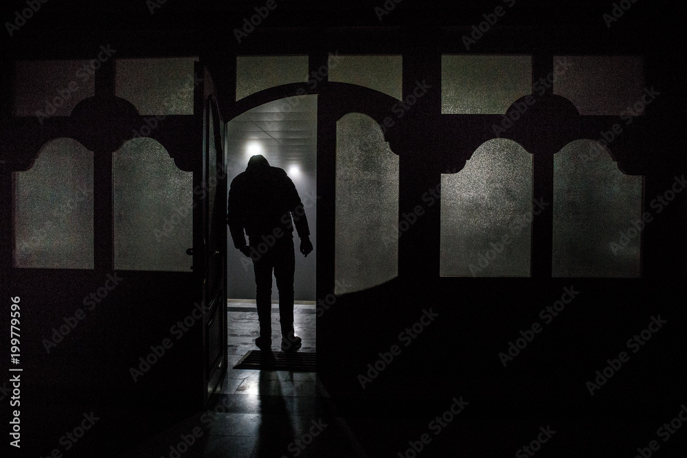 Silhouette of an unknown shadow figure on a door through a closed glass door. The silhouette of a human in front of a window at night. Scary scene halloween concept of blurred silhouette Silhouette of an unknown shadow figure on a door through a closed glass door. The silhouette of a human in front of a window at night. Scary scene halloween concept of blurred silhouette