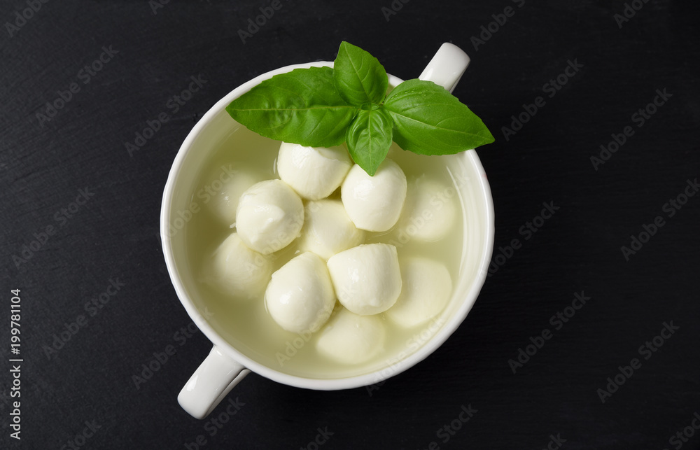 Mini mozzarella with herbs, basil on ablack stone background top view