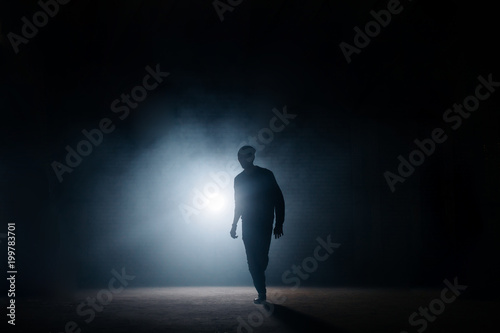 dark silhouette of slim man walking on the street at night. being alone. lighted street. thief sneaking in the street.night crime