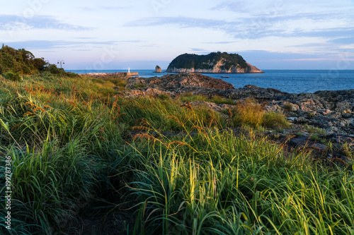 Sunshined grassland and Lighthouse during sunset at Seaseom, Seogwipo, Jeju Island, South Korea photo